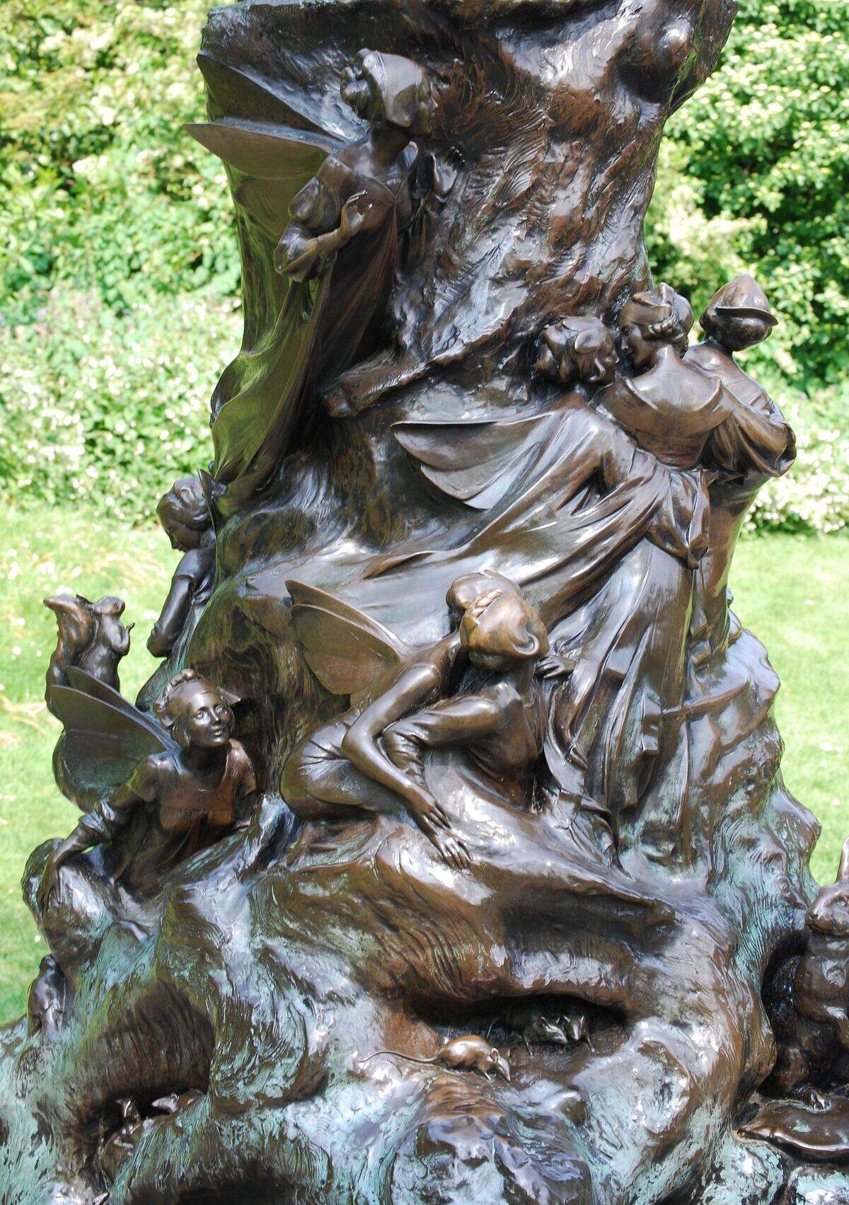 Detail of the Peter Pan statue base showing fairies, mice, and small figures climbing the bronze tree stump.